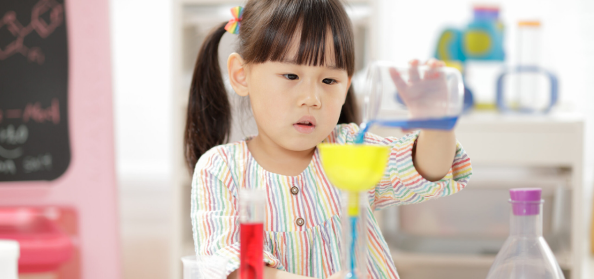 Preschooler pouring and measuring water in a science experiment. 
