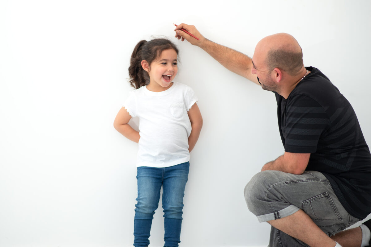 Father measuring his preschool daughter to see how tall she is. 