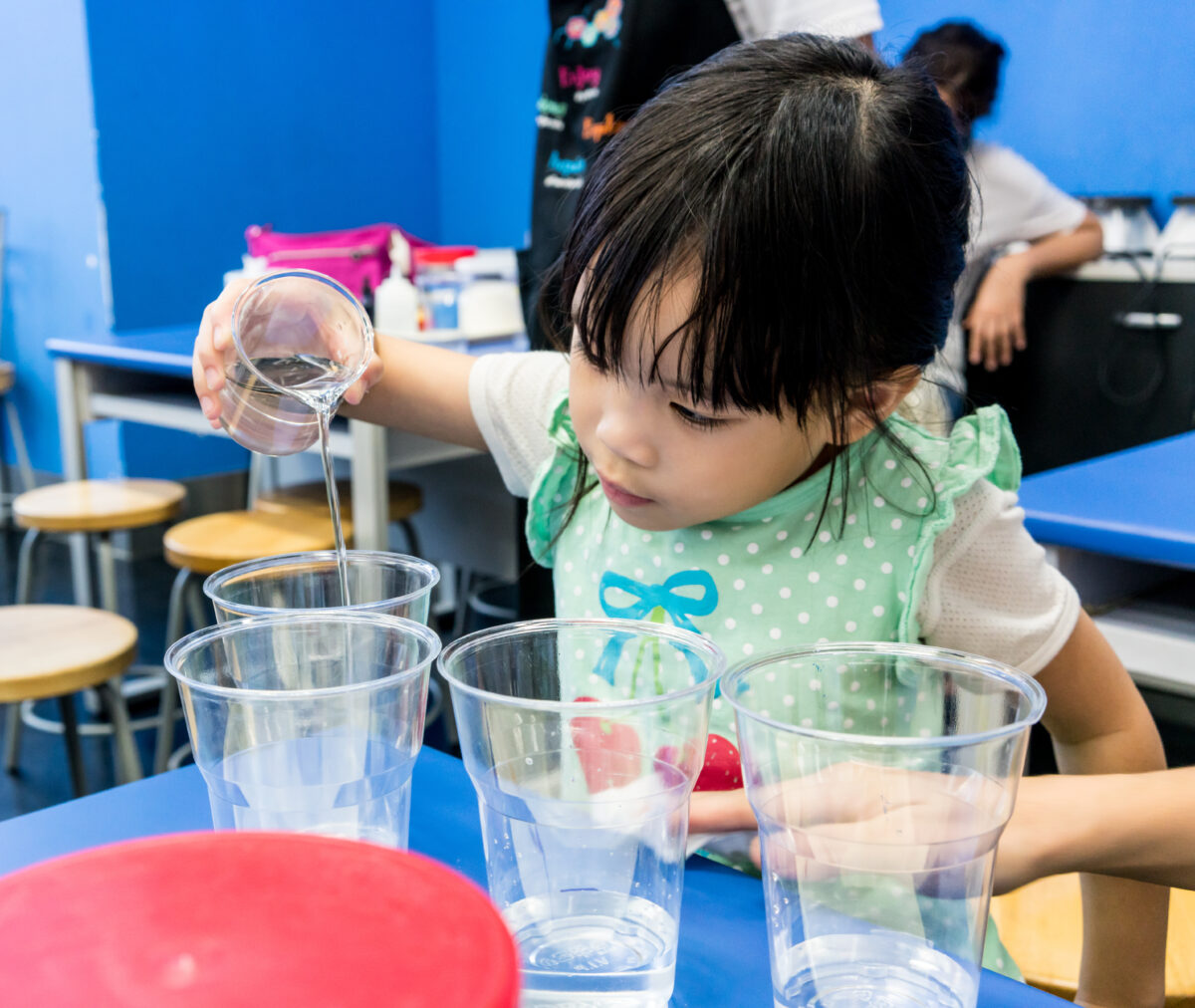 Preschooler measuring liquid from one container to another in a preschool activity. 