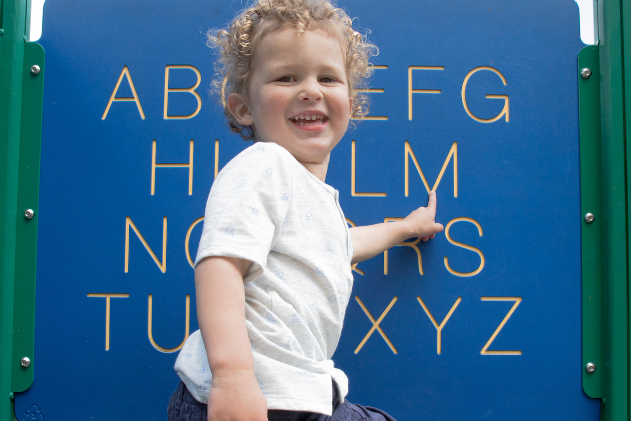 A young preschool age child pointing to letters on a sign at the park. 