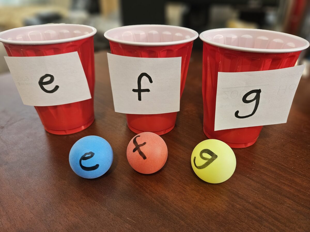 Cups and ping pong balls with letters on them. 
