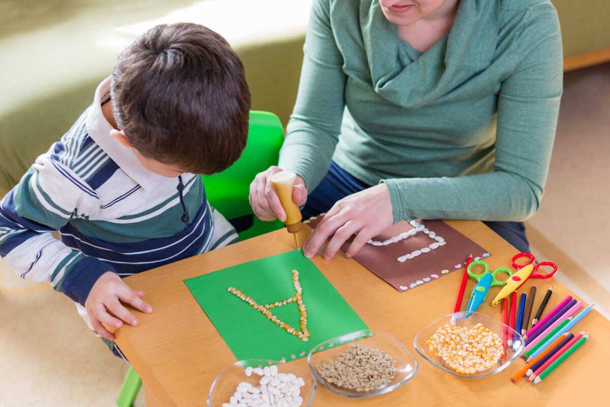 Boy making alphabet book with his teacher. 