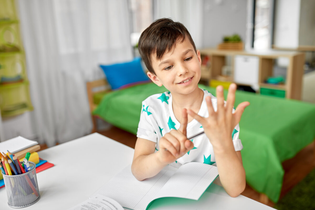 Boy counting his 5 fingers while writing in a notebook. 