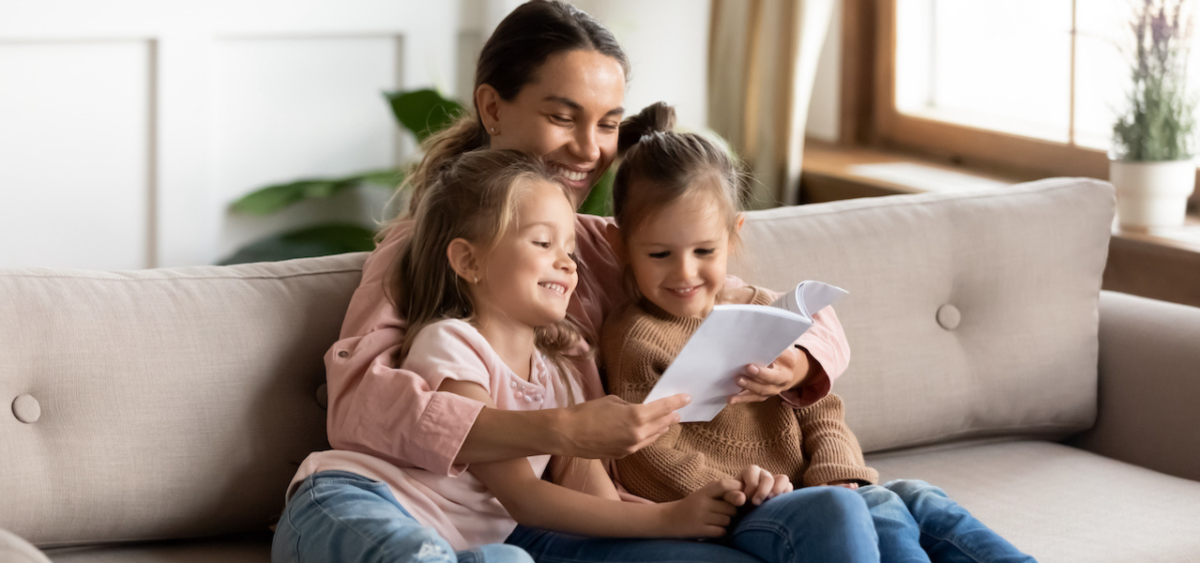 Mother reading to her kindergarten twins sitting on the couch. 