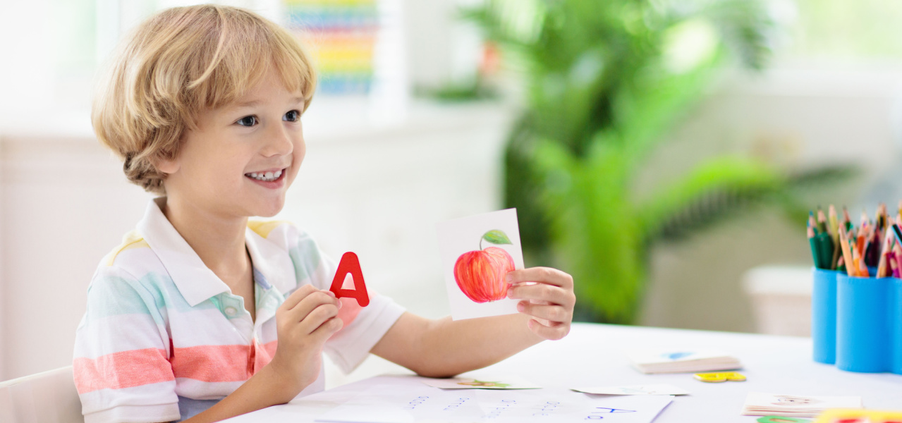 A child holding a letter A alphabet card and a card with a picture of an apple on it. 