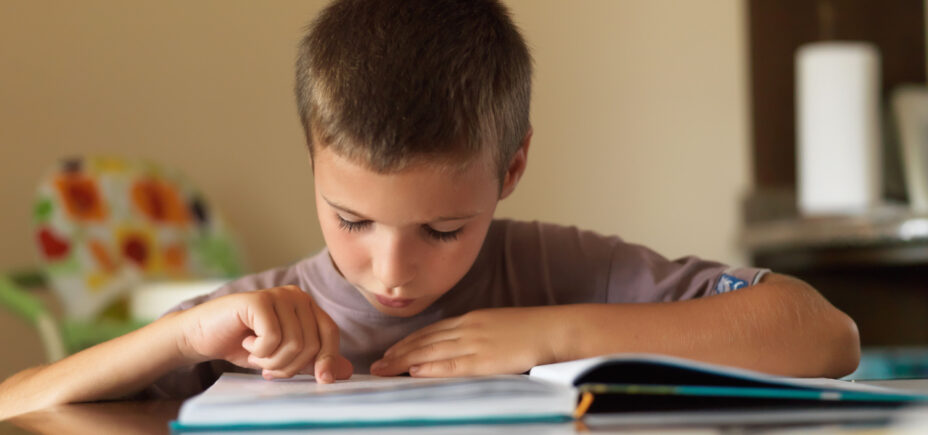 Second grade boy reading out of a book. 