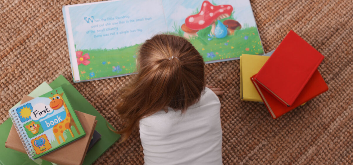 1st grade girl reading a book while laying on the floor. 