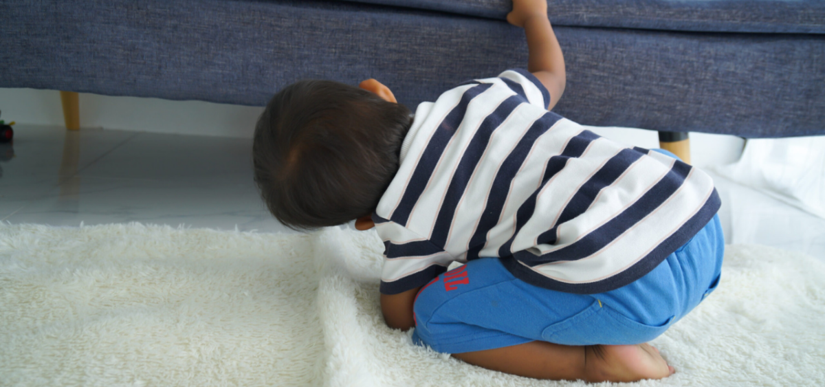 A boy looking under a couch for a missing sight word flashcard. 