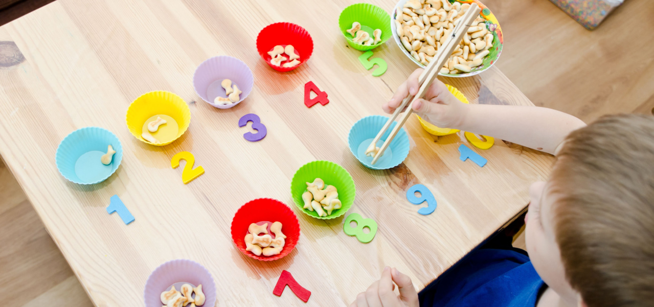 Child practicing math and numbers by counting goldfish in colorful cupcake wrappers. 