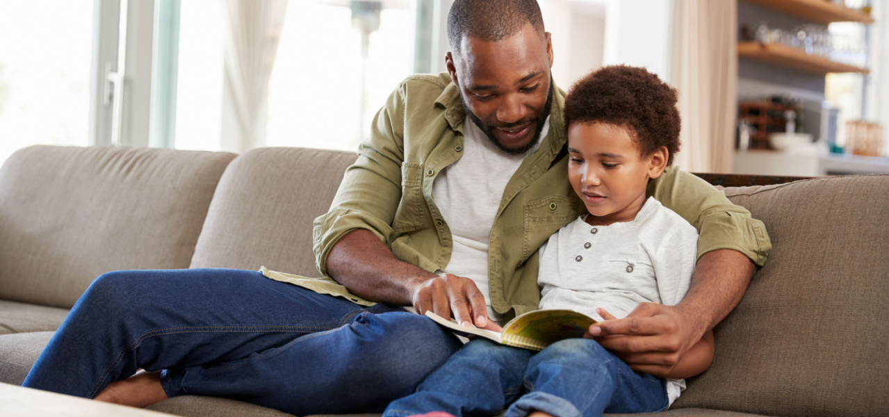 A father reading to his son while sitting on the couch. 