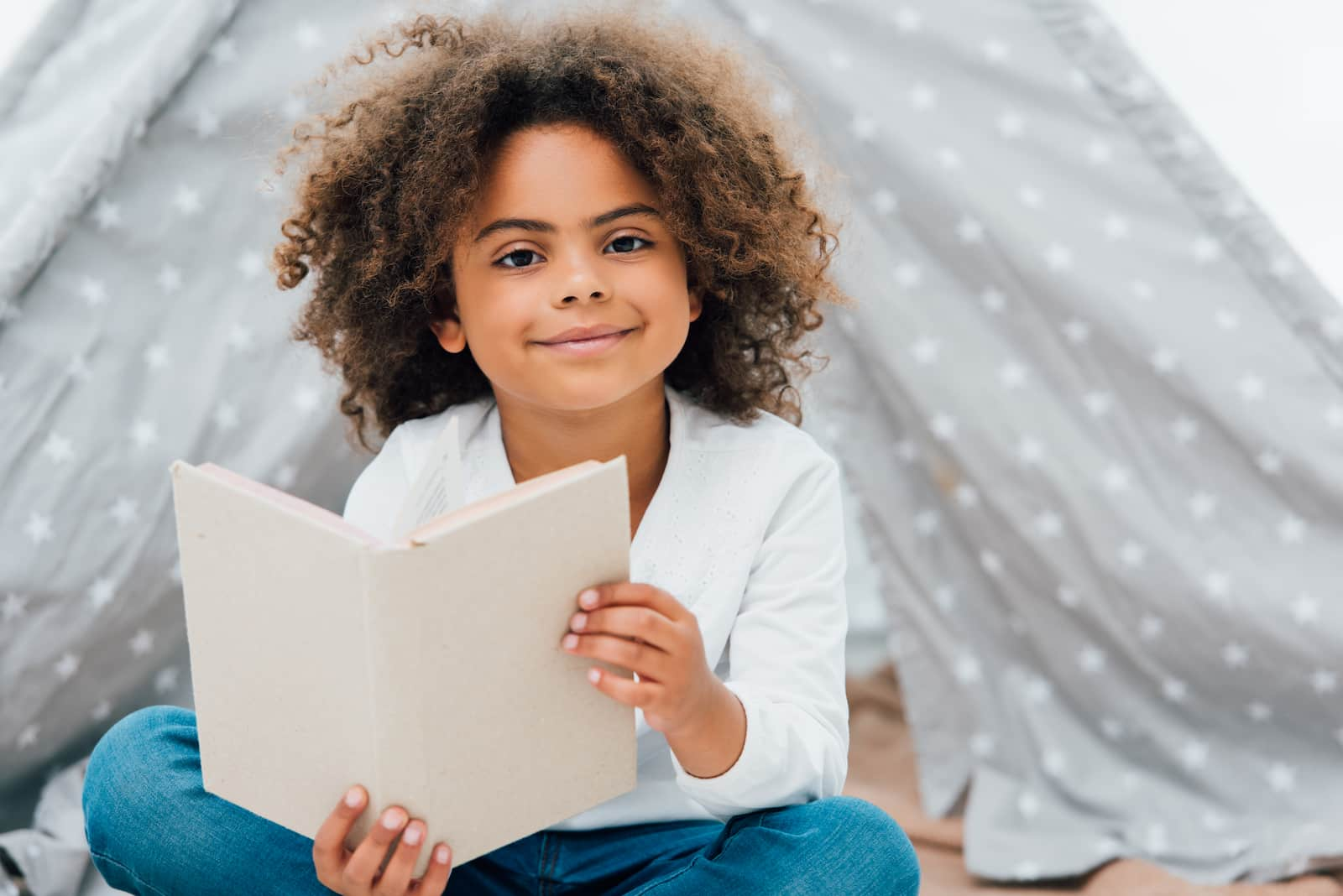 Child sitting in a play tent reading. 