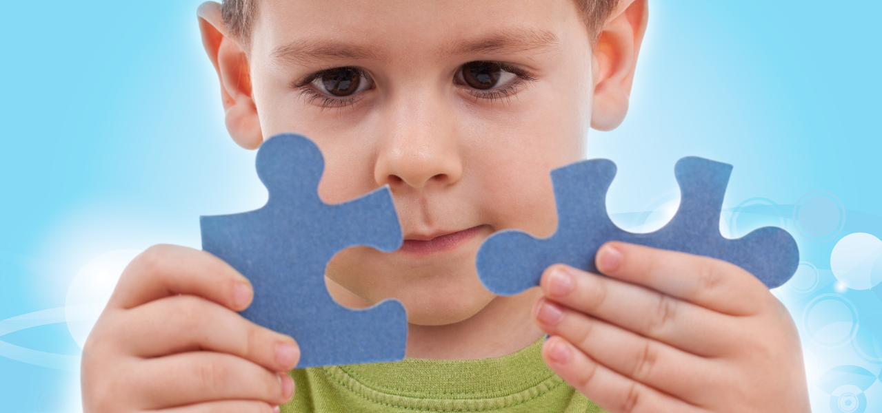 A boy looking at how two puzzle pieces fit together. 