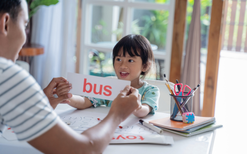 Father, teacher, or tutor, helping a young girl sound out new words from a flashcard. 