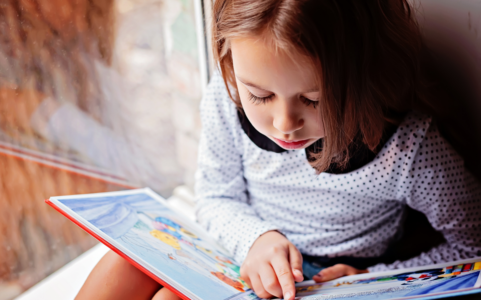 Young girl reading a book while pointing at the words. 