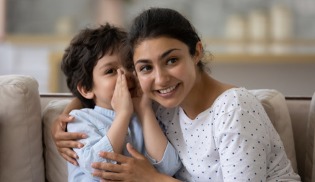 Preschool child whispering in the ear of his caregiver. 