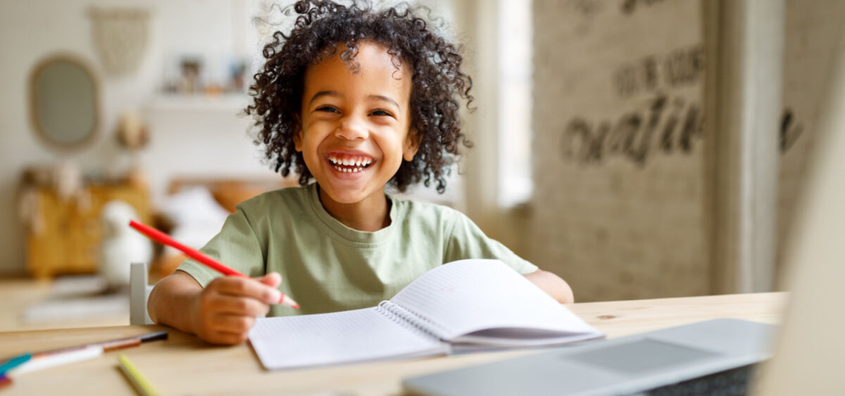 Young boy smiling very happily while writing in a notebook. 