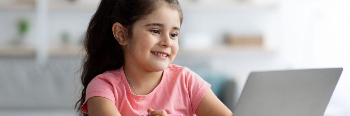 Little girl looking at a laptop screen while smiling. 