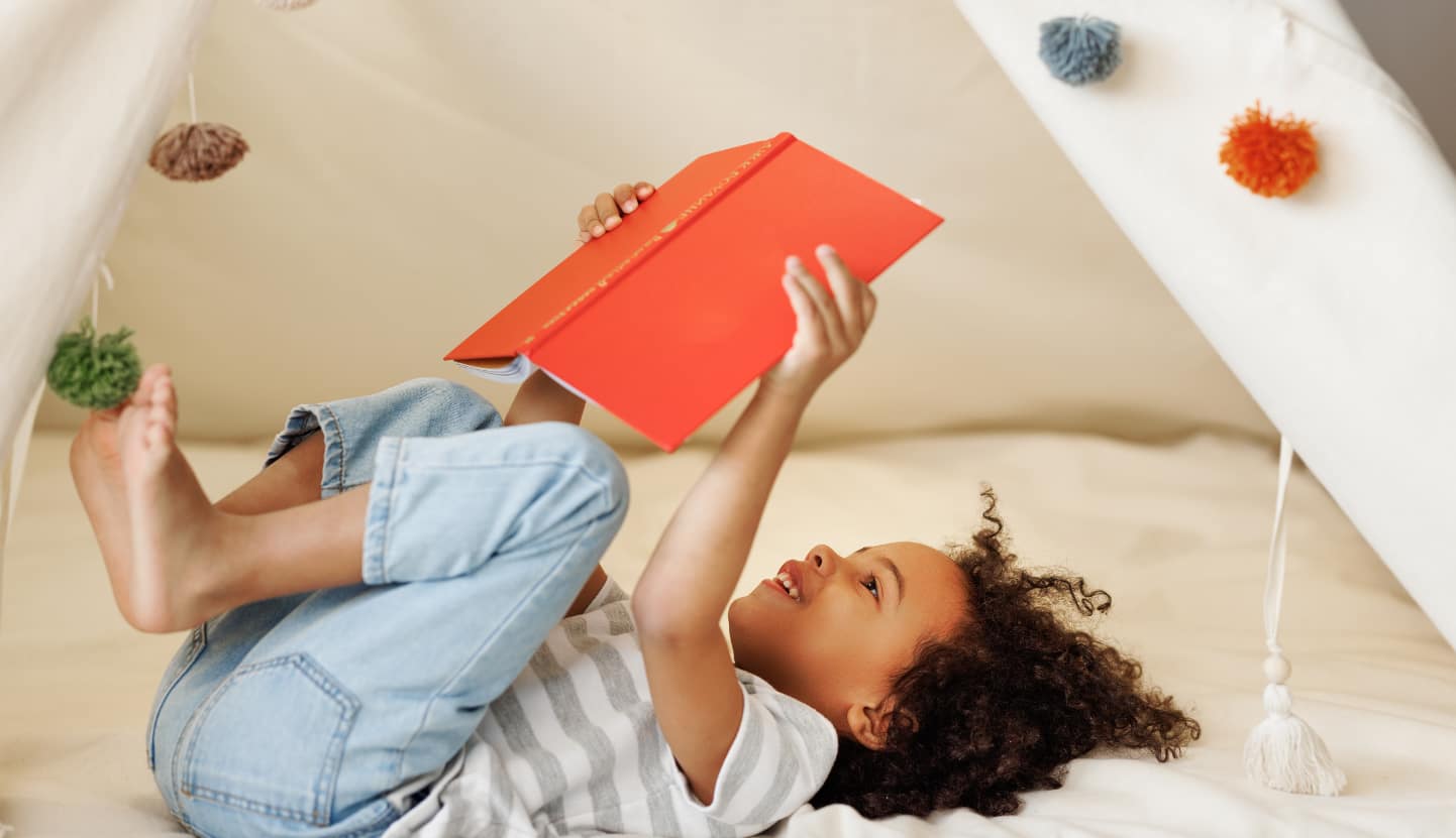 A child laying on their back with a book in the air. 