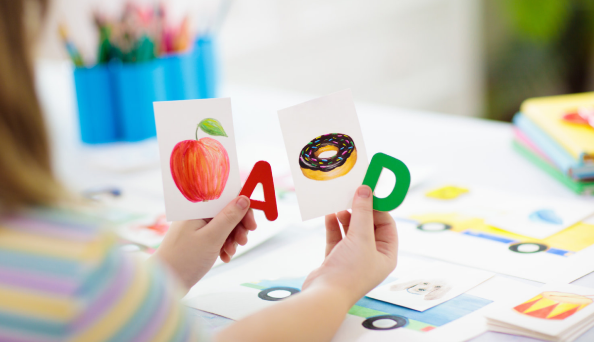 A young child holding the letter a and letter d with cards that have a picture of an apple and donut. 