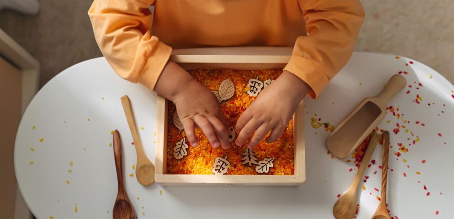 A child playing with colorful rice sensory bin. 