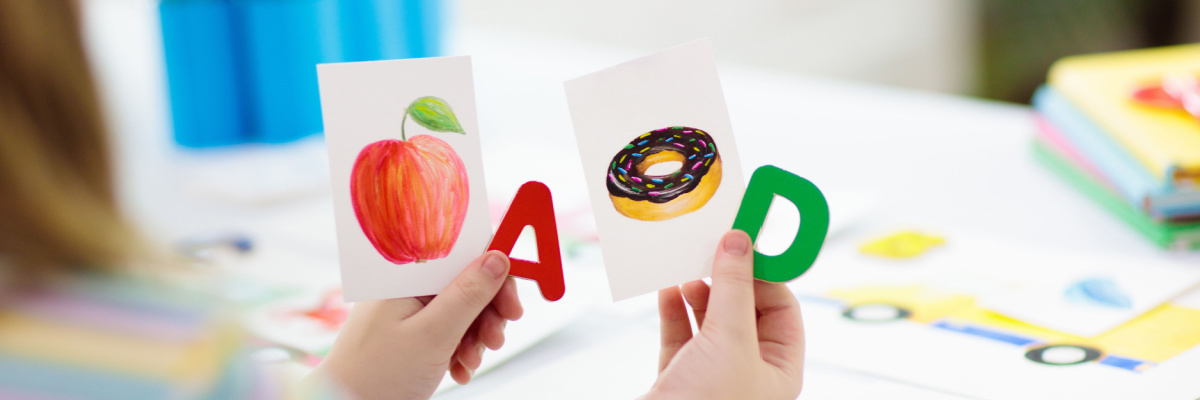 Child holding flashcards of the letter A with a picture of an apple and a letter D with a picture of a donut to learn phonics. 