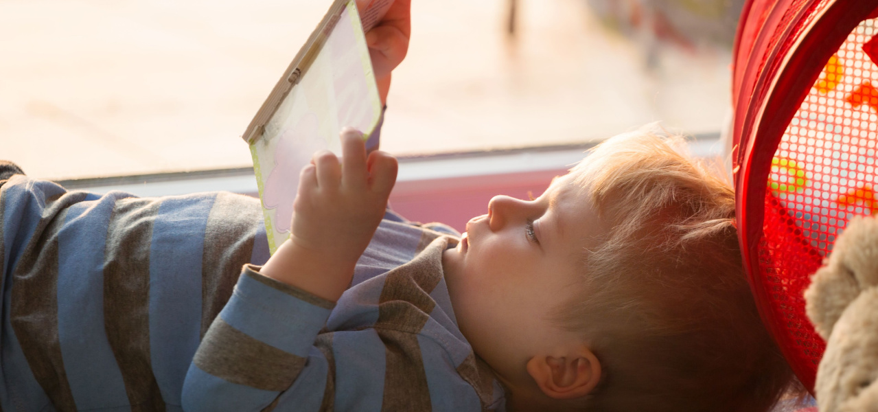 Preschool child laying on his back while reading a book. 