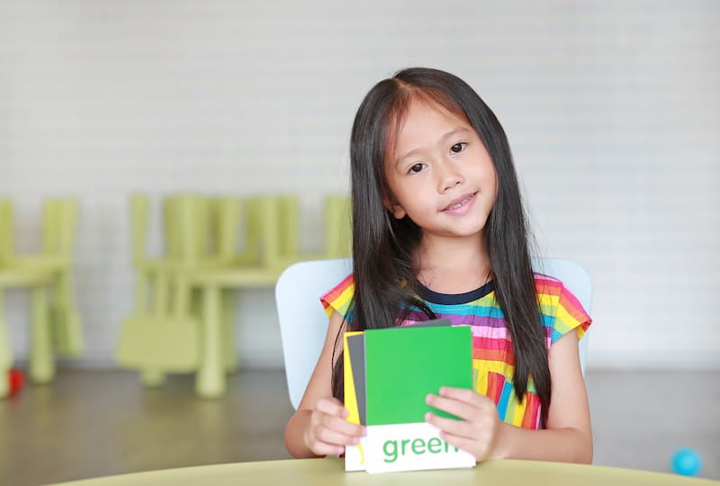 A girl holding sight word flash cards, learning how to read color words. 