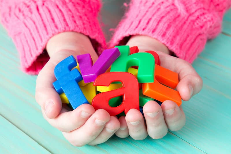 A child holding colorful magnetic letters it their hands. 