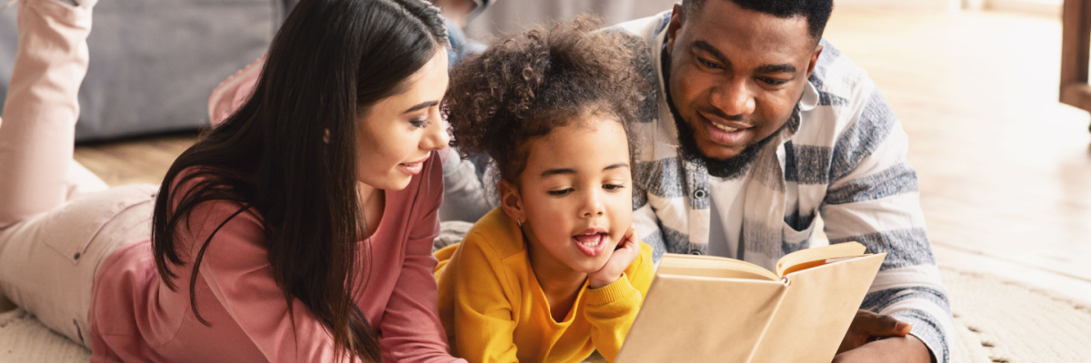 Parents teaching their daughter how to read by reading together. 