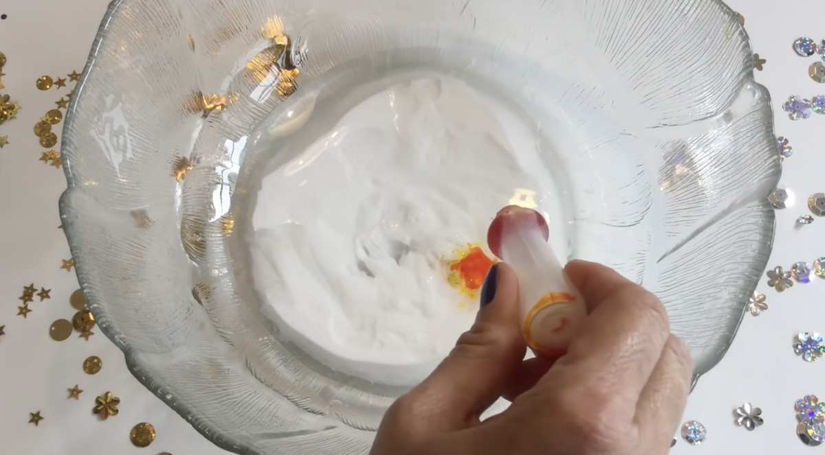 Adding drops of food coloring to a bowl of glue and shaving cream. 