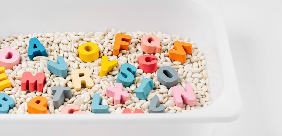Colorful alphabet letters in a bin of beans for sensory exploration. 