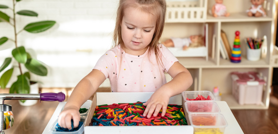 A preschool age child looking through a bin of colorful noodles. 
