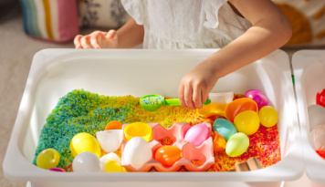 Colorful rice in a plastic bin with Easter eggs. 