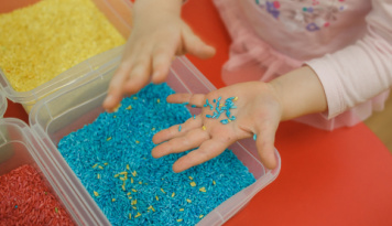 A child holding a handful of colorful blue rice. 