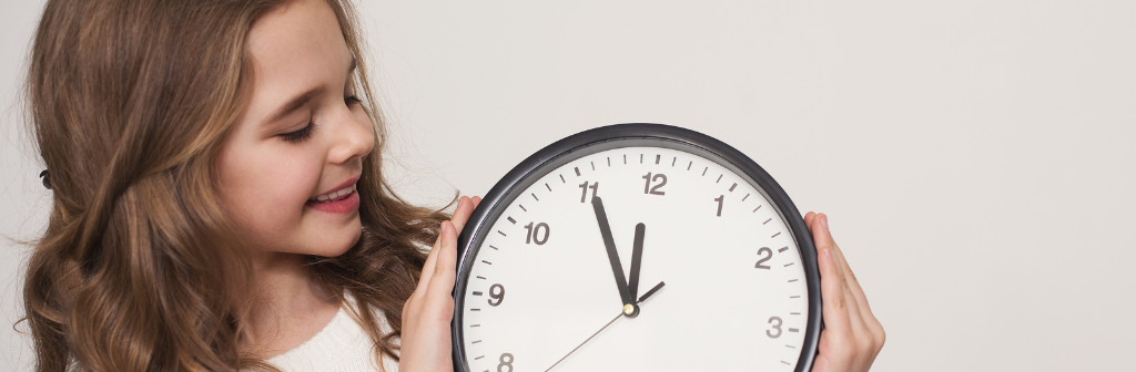 Little girl holding a clock and looking at it. 