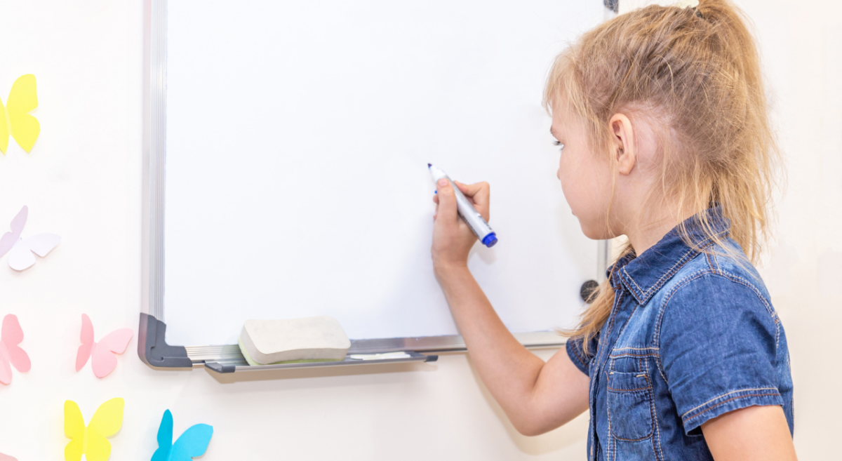 A young girl getting ready to write on a dry erase board. 