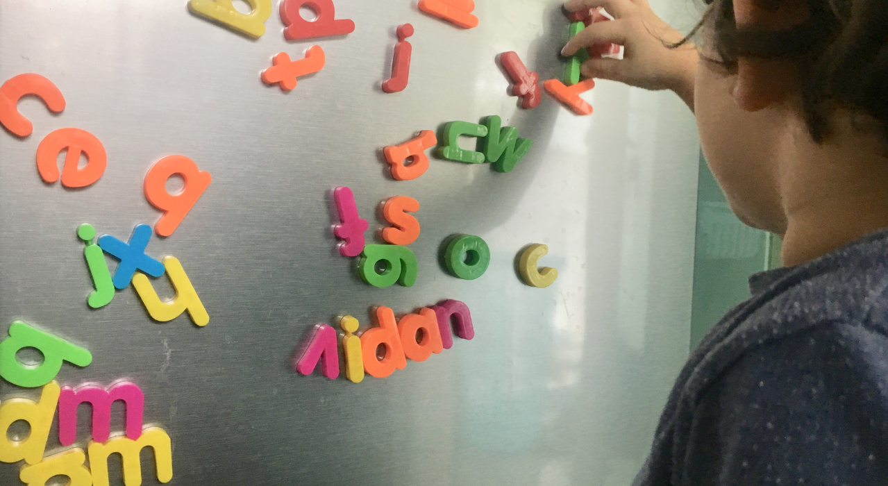 A child moving around magnetic letters on a fridge. 