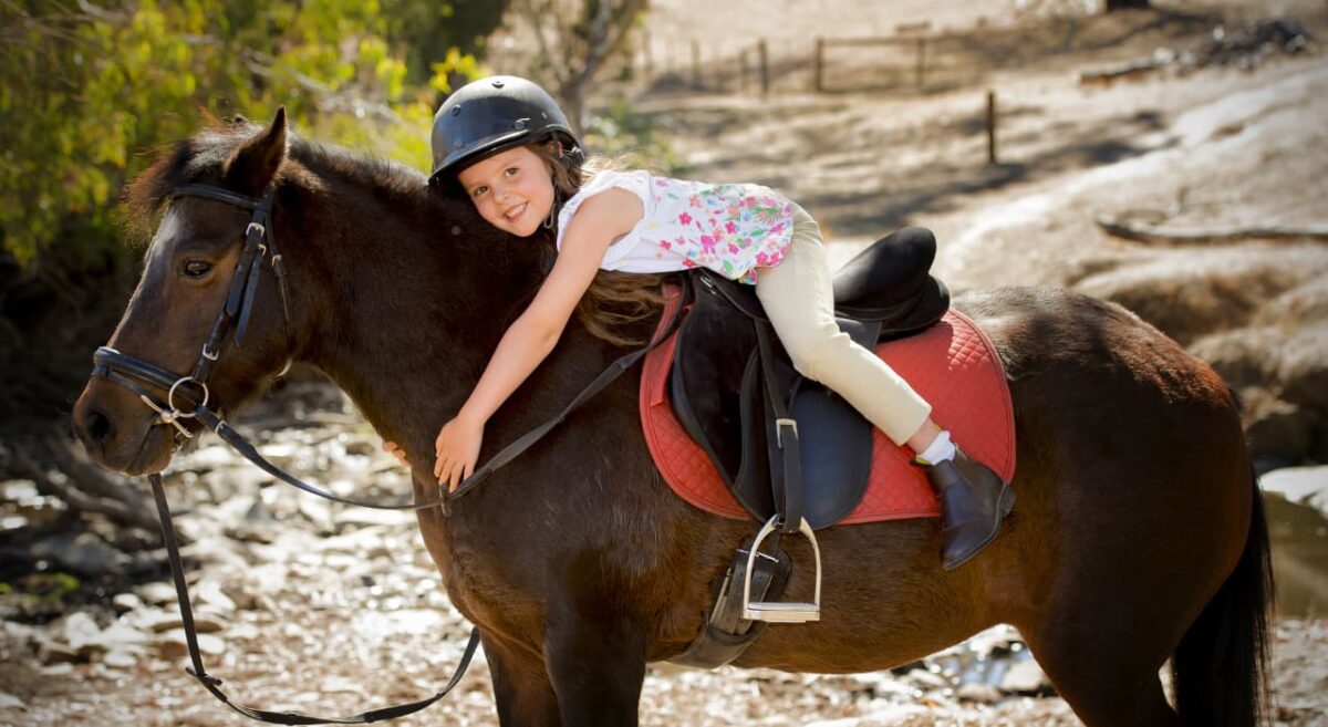Girl sitting on top of a horse hugging it. 
