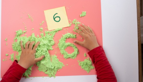 A child playing with kinetic sand making numbers. 