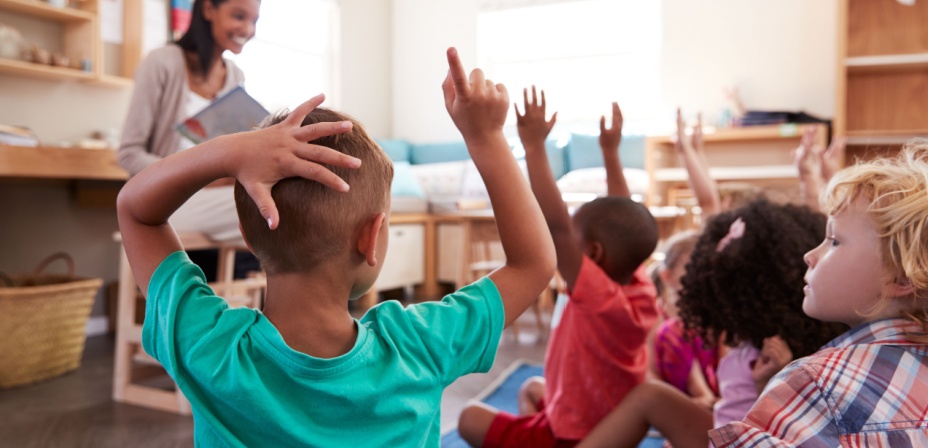 Children raising their hands to answer questions about a reading topic. 