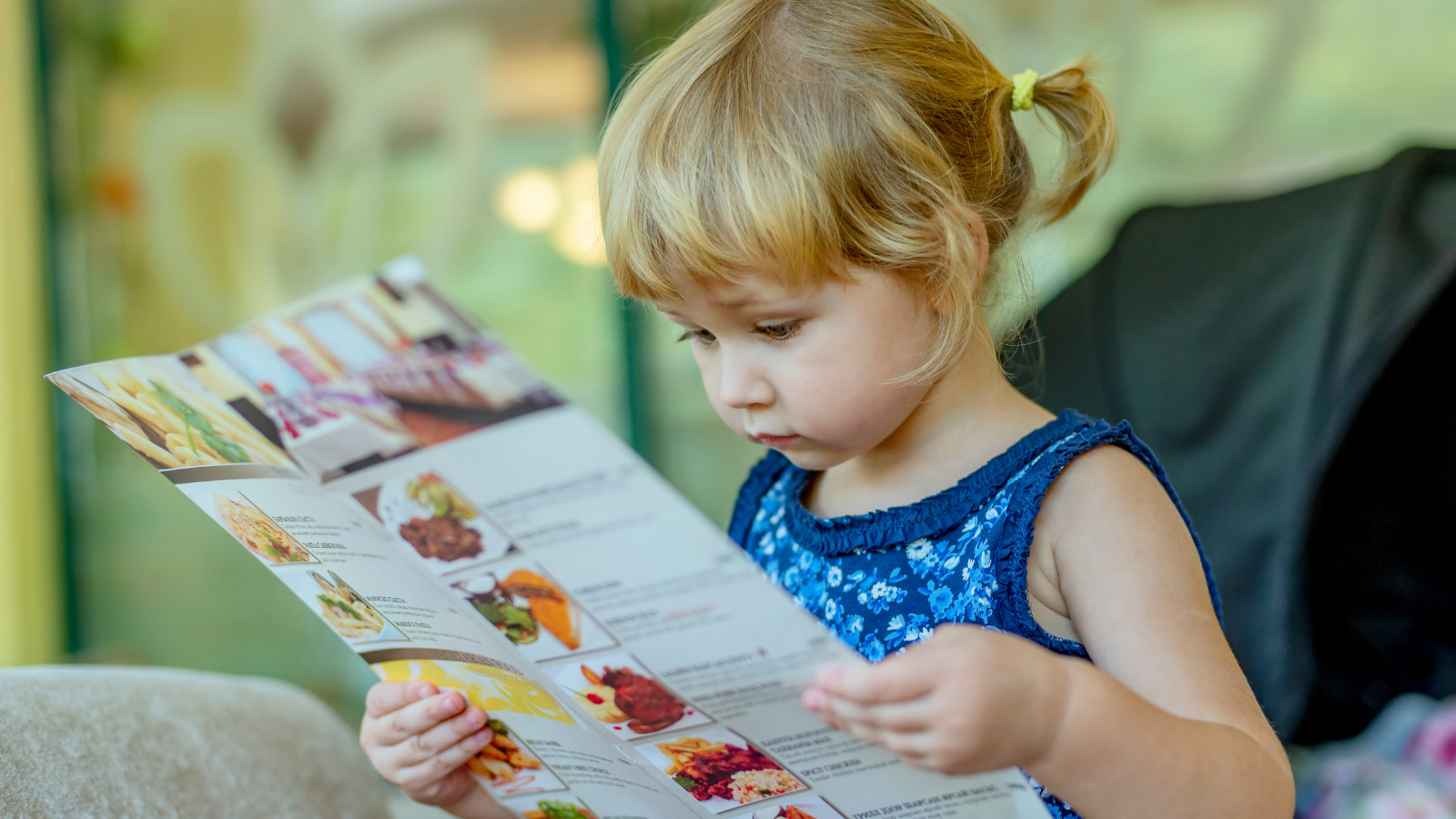 A young child sits on a couch and looks through a colorful educational workbook during a back-to-school learning activity.