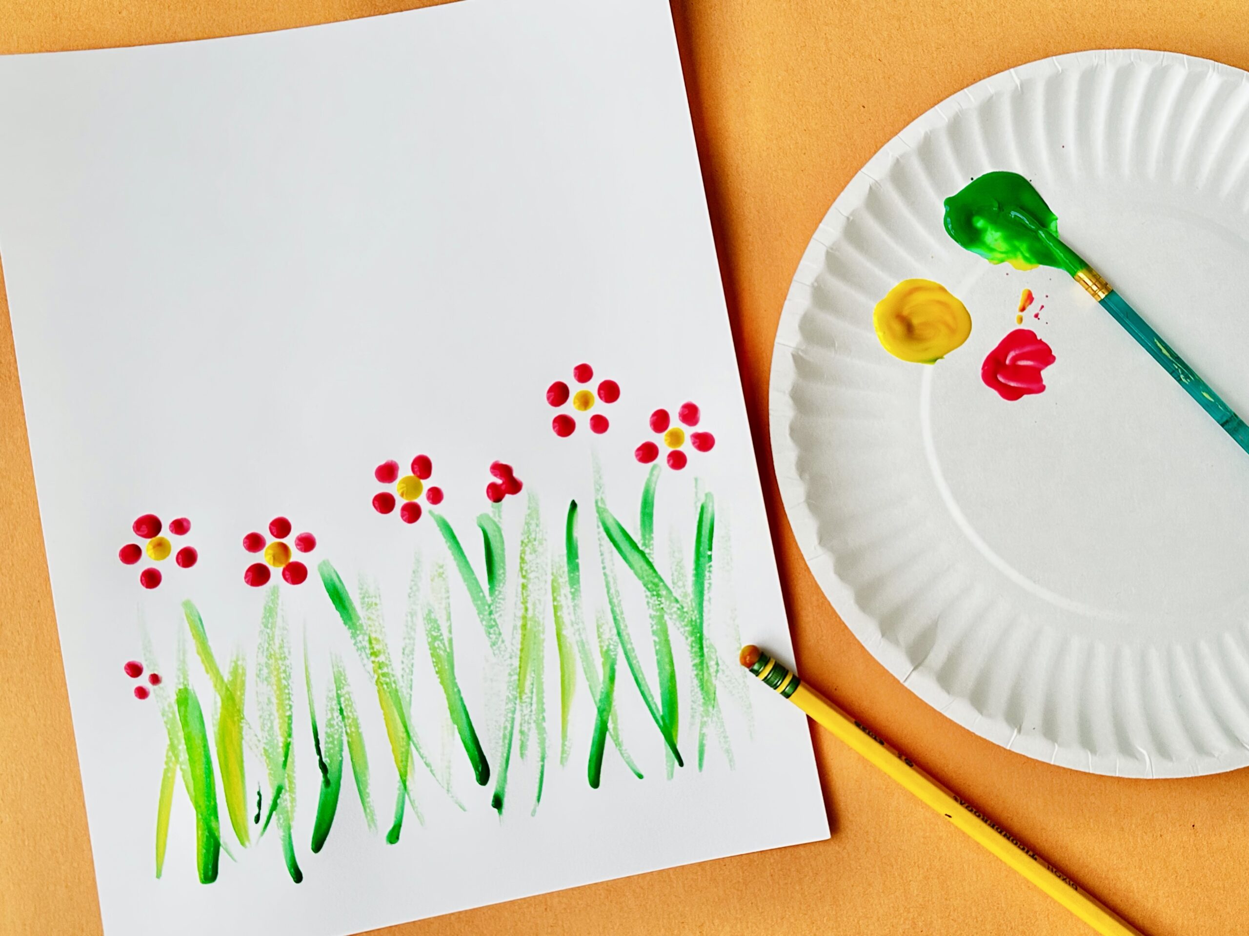 Child’s painting of green grass with small red and yellow flowers using finger or dot painting technique.
