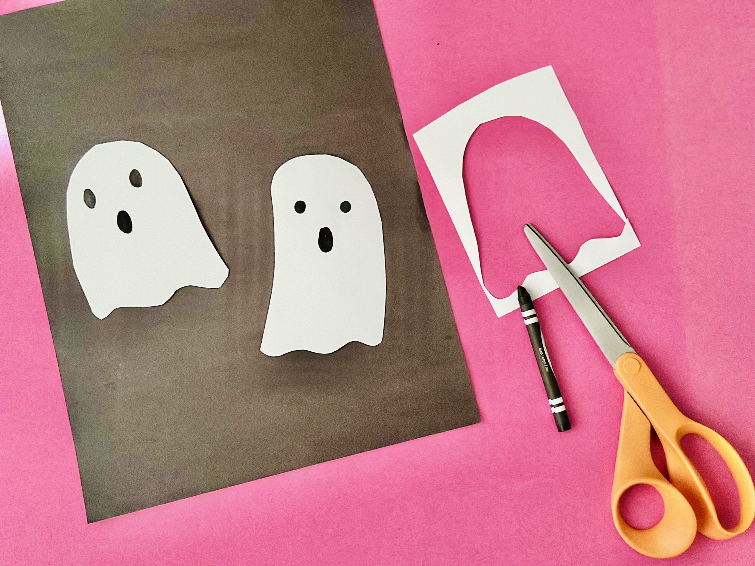 Simple white paper ghosts being cut out with scissors for a Halloween craft.