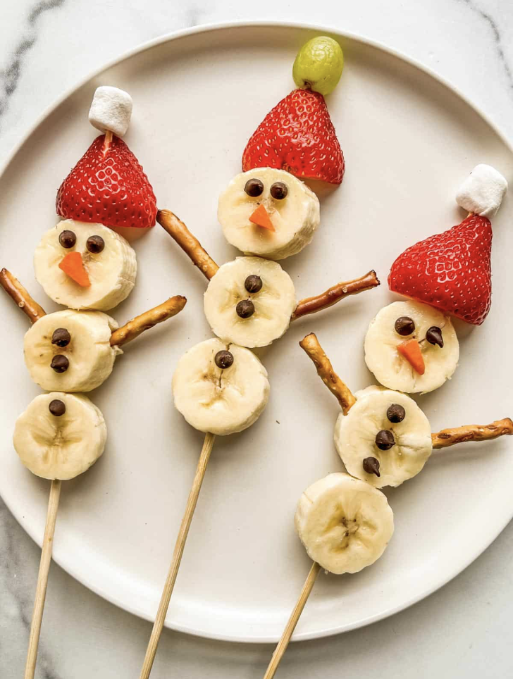 Cute food snowman made of bananas, pretzels, chocolate chips, strawberries, and marshmallows.