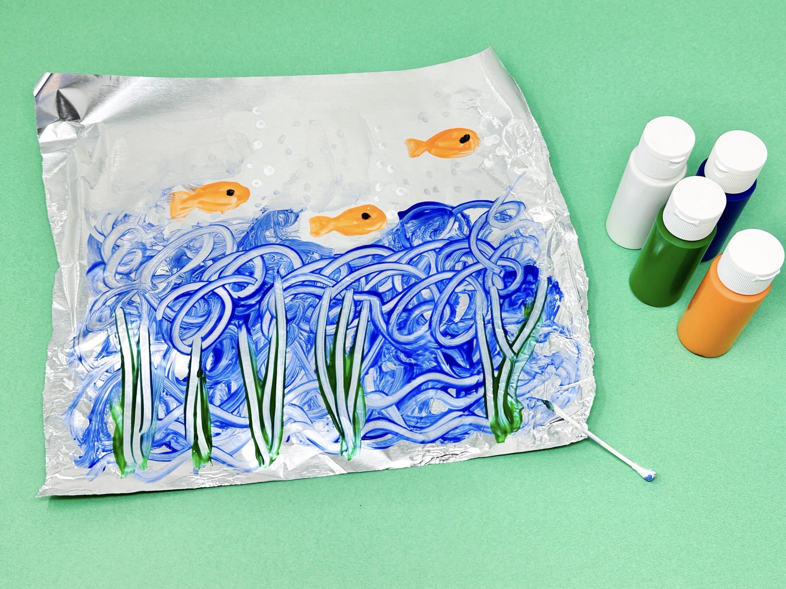 Ocean scene painted on aluminum foil with blue waves and orange fish.
