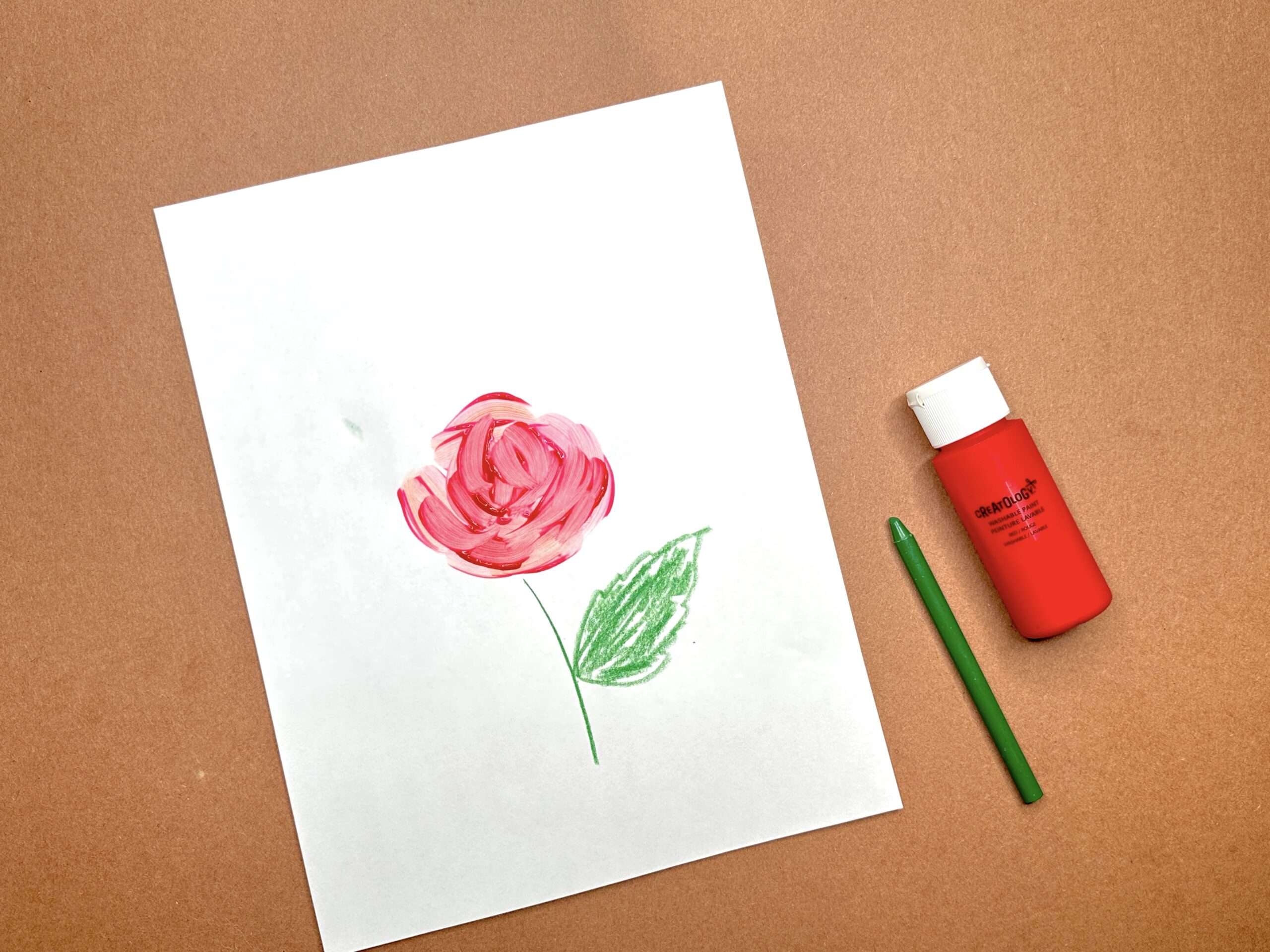 Simple painted red rose with green leaf on white paper, with paint bottle and brush nearby.