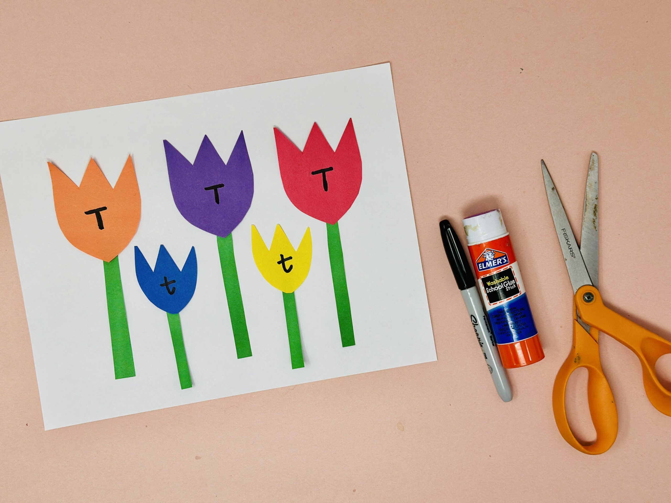Paper tulip flowers in different colors with letters written on each petal, alongside scissors and glue.