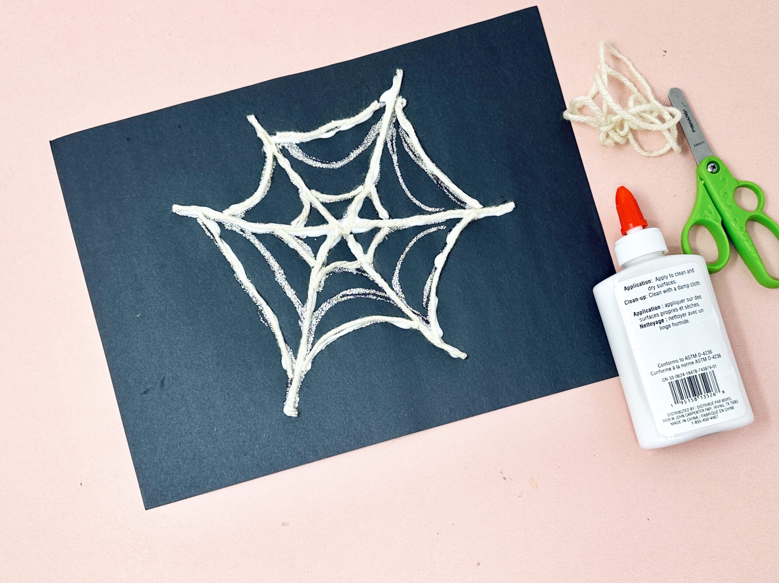 Spider web Halloween craft made with white yarn glued onto black paper.