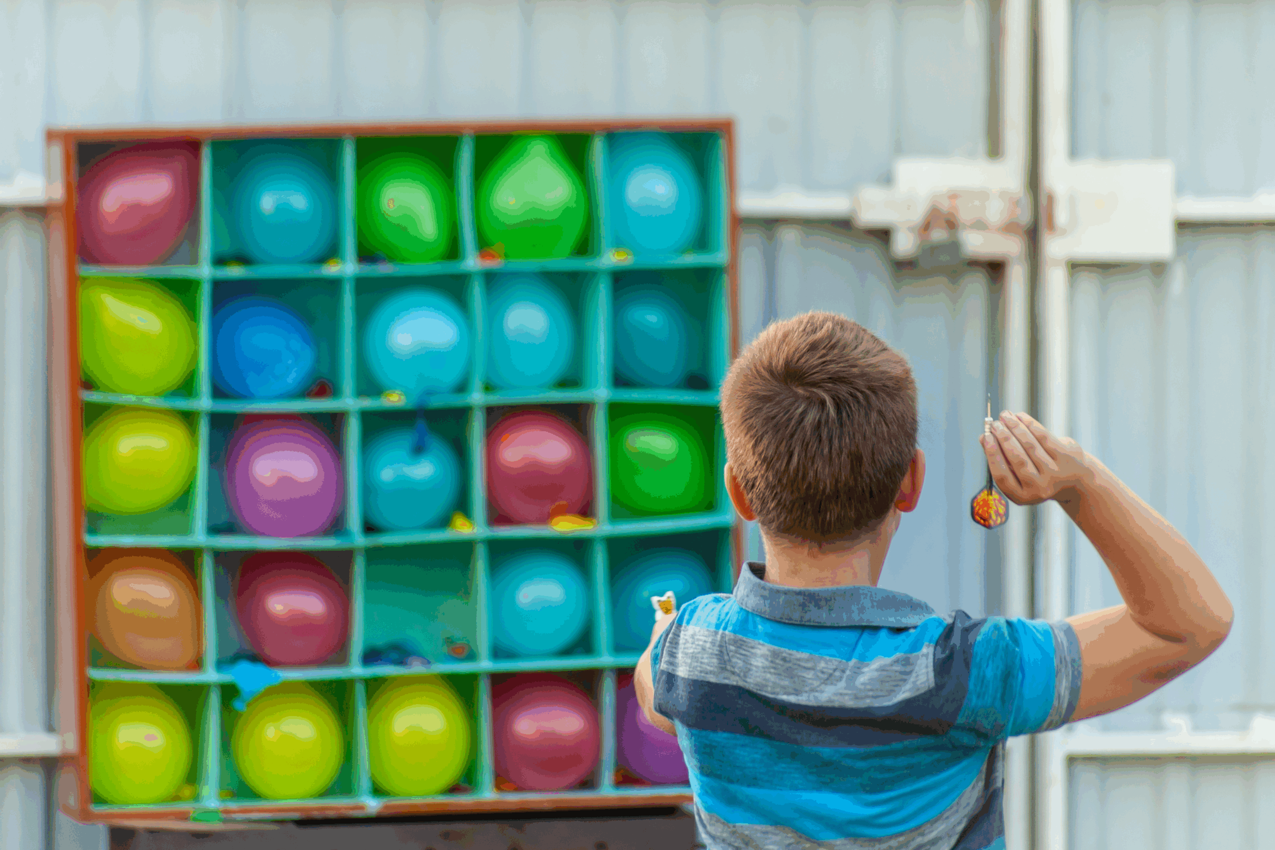 Boy throwing darts at a balloon in this fun summer backyard carnival activity idea. 