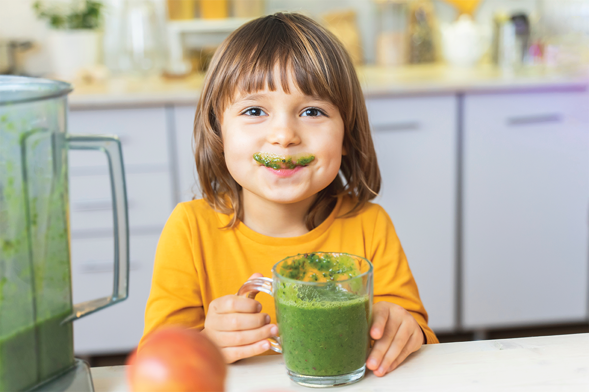  A young child drinking a homemade green smoothy for a fun summer activity. 